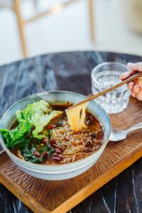 Delicious noodle soup with chopsticks and fresh greens in a ceramic bowl on a wooden tray.