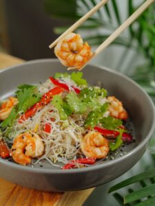 Close-up of a shrimp and rice noodle dish garnished with herbs and spices.