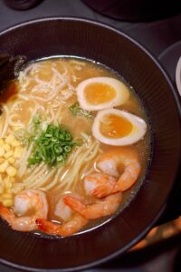 Mouthwatering shrimp ramen with soft-boiled egg, corn, and scallions in savory broth.