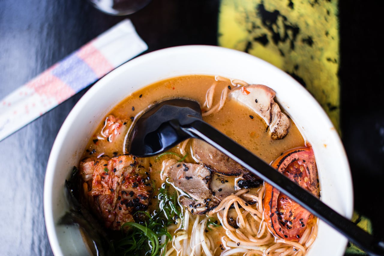 High-angle view of pork ramen with vegetables and sesame seeds in a white bowl.